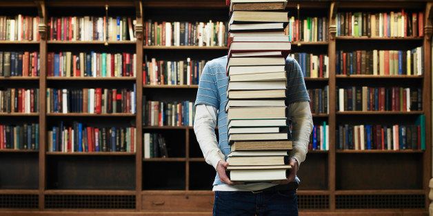 Young man carrying stack of books in university library