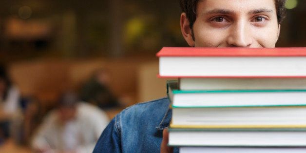 Student holding books in front of face in library, portrait