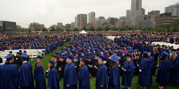 Graduates line up to receive their diplomas under cool and cloudy skies with the skyline of Denver as their backdrop. Metropo
