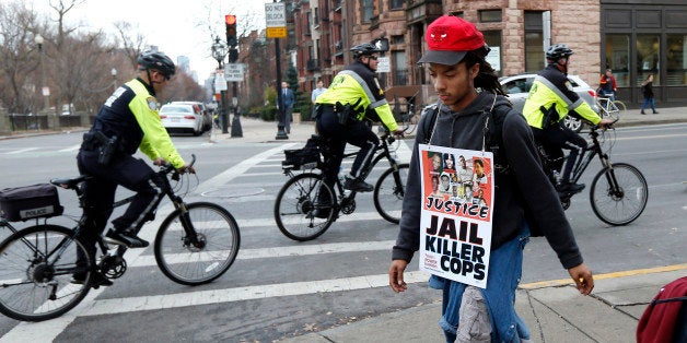 Boston Arts Academy student, Michael Cordero, 18, walks as police ride by on bicycles during a march in Boston, Monday, Dec. 1, 2014, to show solidarity with protesters in Ferguson, Mo. Students and others are joining a nationwide series of protests over a white police officer's shooting of a black Missouri teenager. (AP Photo/Elise Amendola)