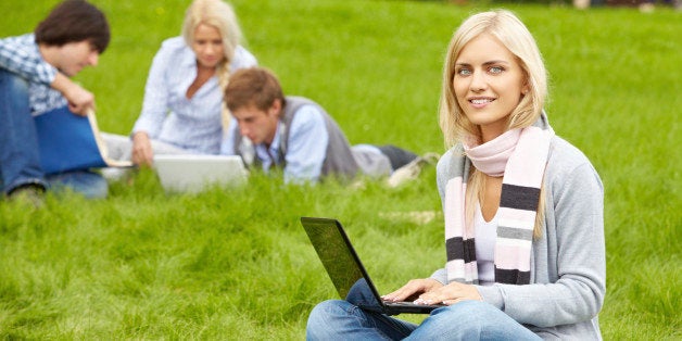 'Beautiful girl studying with laptop on grass, looking at camera and smiling'