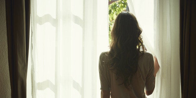 Young woman peeking out from net curtains