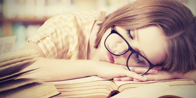 tired student girl with glasses sleeping on the books in the library
