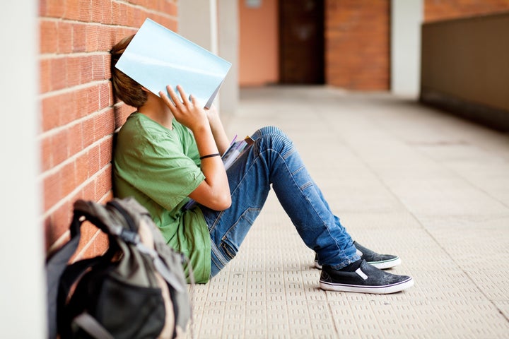 tired high school student using book cover his face