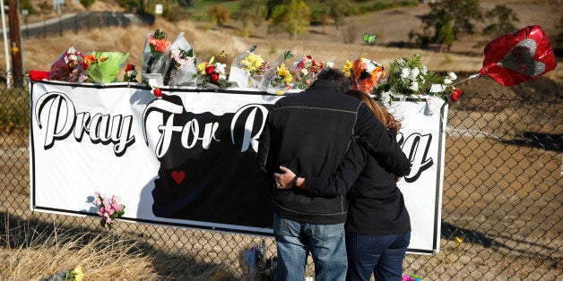 Charley Thompson, left, and his wife Rachel Thompson embrace as they place flowers at a makeshift memorial near the road leading to Umpqua Community College, Saturday, Oct. 3, 2015, in Roseburg, Ore. Armed with multiple guns, Chris Harper Mercer walked in a classroom at the community college, Thursday, and opened fire, killing several and wounding several others. (AP Photo/John Locher)