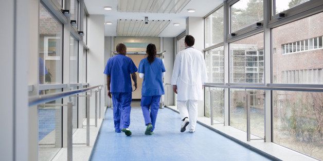 Three medical professionals walking together down a corridor in a hospital, rear view