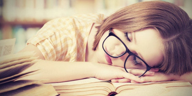 tired student girl with glasses sleeping on the books in the library