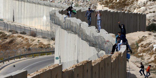 Palestinian demonstraters stand on top of the Israeli controvertial separation wall separating the West Bank city of Abu Dis (R) from east Jerusalem, during clashes with Israeli security forces, on October 28, 2015. AFP PHOTO / AHMAD GHARABLI (Photo credit should read AHMAD GHARABLI/AFP/Getty Images)