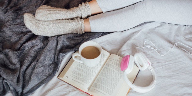 Women resting leg in bad enjoing in reading book, drinking coffee and listening music.