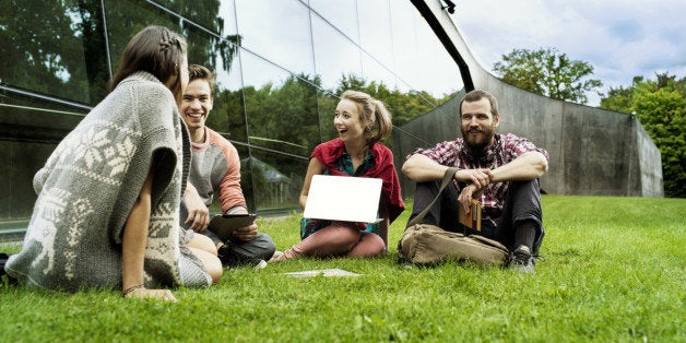 Four students sitting on the grass in front of a big modern university building