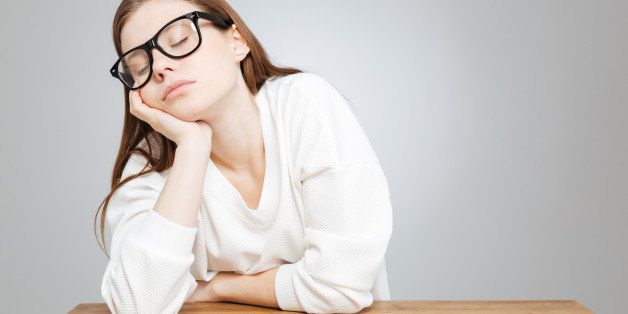 Tired lovely teenage girl in glasses sitting and sleeping at the table