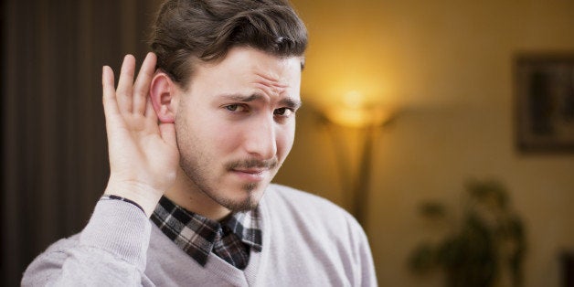 Handsome young man can't hear, putting hand around his ear. Indoors shot inside a house