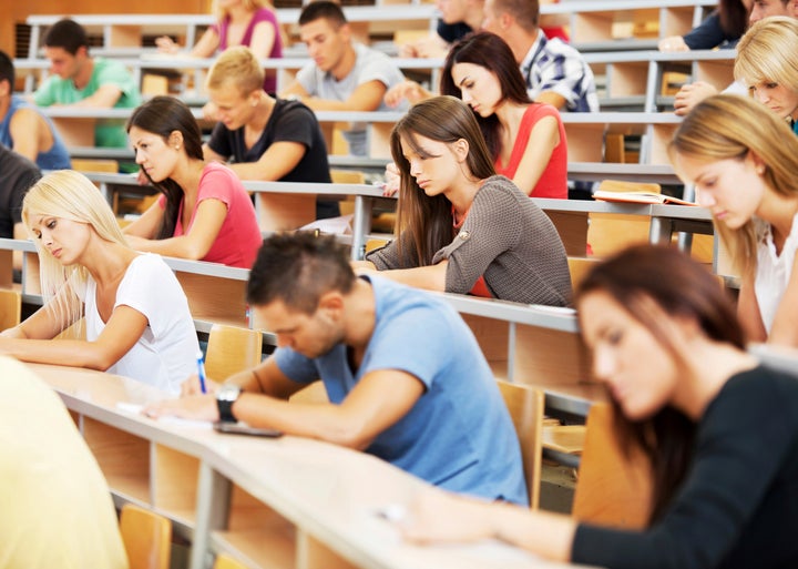 Group of college students in the university amphitheatre, they are sitting and doing an exam. 