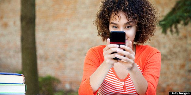 Ethnic female student with curly hair wearing wearing an orange shirt and texting with her smart phone