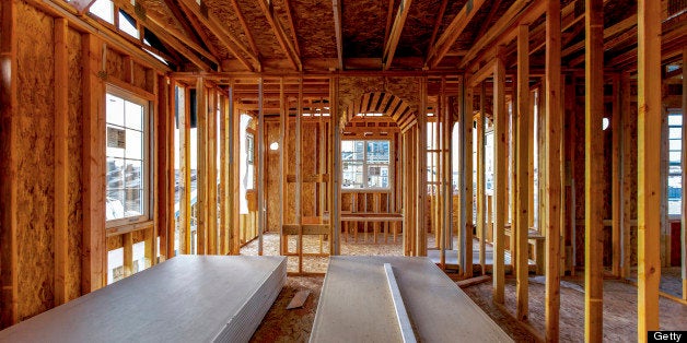 The interior of a building still under construction. Wood studs showing, no walls complete. Looking out through newly installed windows to a view.