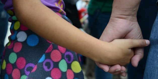 A woman and her daughter hold hands as she speaks to the press upon arriving in San Pedro Sula, about 260 km north of Tegucigalpa, on July 14, 2014 after being deported from the United States. A first group of 120 deportees from Honduras, El Salvador and Guatemala who had crossed into the United States illegally were repatriated by plane to their countries -- most of them unaccompanied youths. US authorities have detained some 57,000 unaccompanied minors since October, twice the number from the same period a year ago, seeking to illegally cross into the US from Mexico. AFP PHOTO/Orlando SIERRA (Photo credit should read ORLANDO SIERRA/AFP/Getty Images)