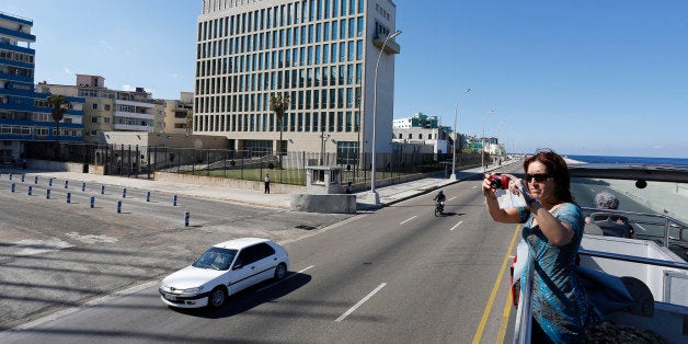 In this Dec. 18, 2014 photo, a tourist takes pictures from a double decker sightseeing bus as she passes the U.S. Interests Section building0 in Havana, Cuba. As Cuba and the U.S. announced the renewal of full diplomatic ties, a small number of Americans were already strolling the cobblestone streets of Old Havana, attending concerts and architecture talks on tightly scripted cultural tours that cost more than some used cars. (AP Photo/Desmond Boylan)