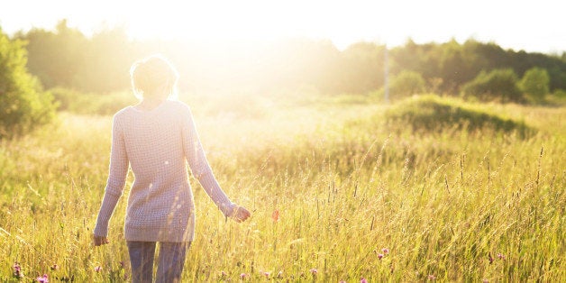 Young woman walking in the field toward the sun holding a poppy flower.