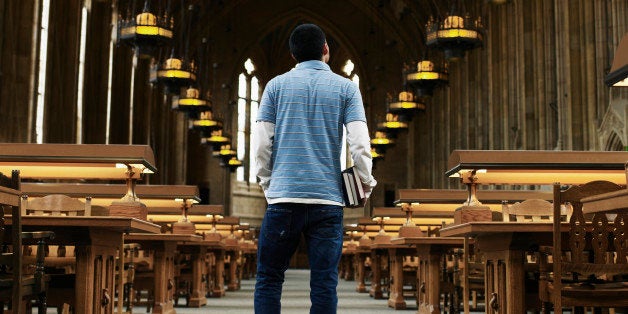 Young man standing in university library, rear view