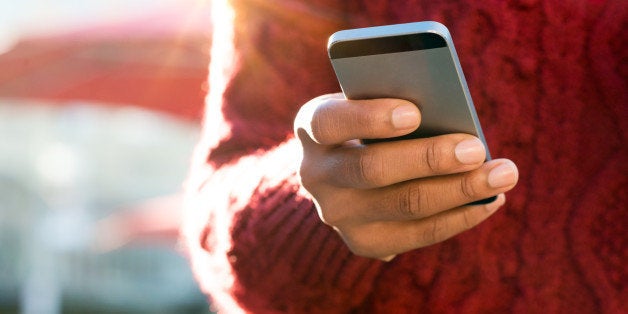 Close up of a young woman's hand typing text message on her smartphone. African young woman is typing on touch screen mobile phone. Close up of female hand texting a message phone outdoor.