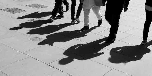 Shadows of six walking pedestrians projected on the sidewalk. Black and white.