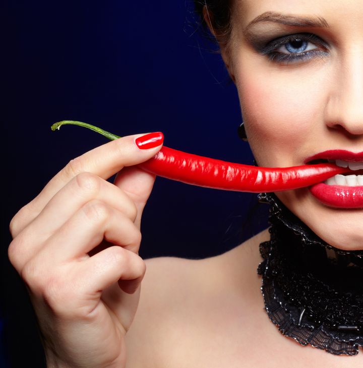 portrait of beautiful brunette girl biting spicy hot red cayenne chili pepper