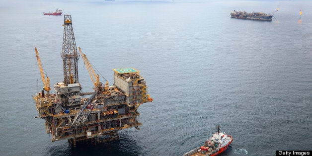 Aerial photo of an offshore oil field with a large fixed oil rig, two FPSO vessels, and numerous support and supply vessels of various sizes. 