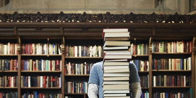 Young man carrying stack of books in university library