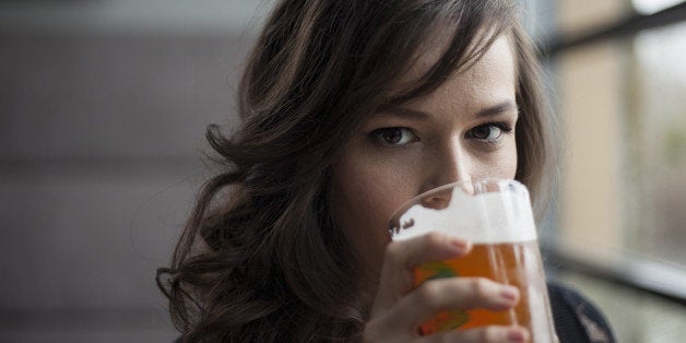 Portrait of a young woman drinking a pint glass of beer.