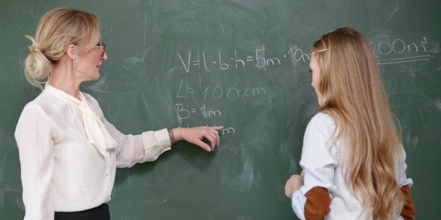 Nordic Education: teacher demonstrates a mathematical formula to a pupil at the chalk board.