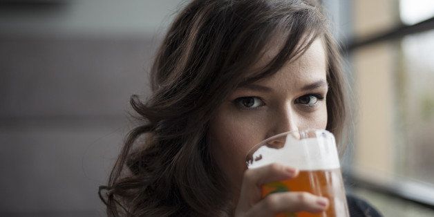 Portrait of a young woman drinking a pint glass of beer.