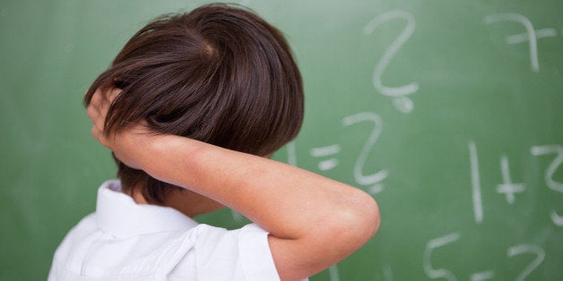 Schoolboy thinking while scratching the back of his head in front of a chalkboard