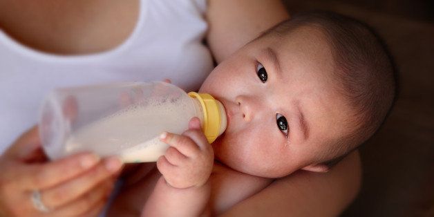 A four month old baby is drinking a bottle in his mother's arms.