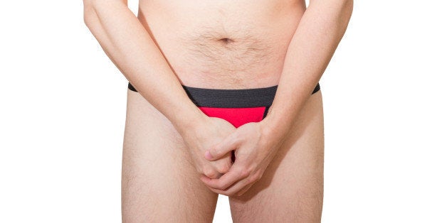 Adult man in black&red underwear holding/hiding/protecting his penis, isolated on white background.