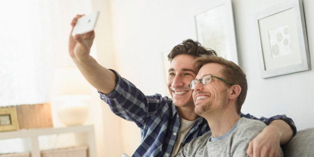 Caucasian gay couple taking selfie on sofa