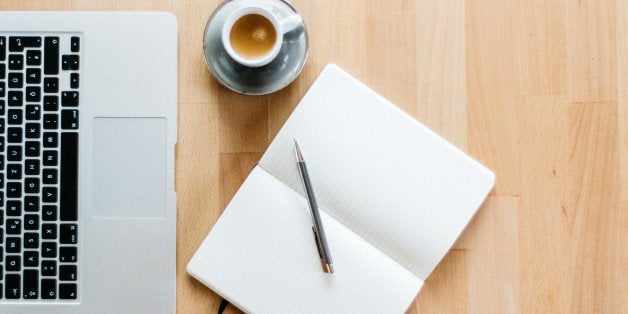A photo of a workspace with a Laptop, an espresso and a notebook with a pen. The photo is taken from directly above and the w