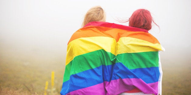 Blonde and redhead woman wrapped in rainbow flag