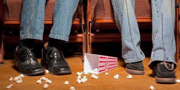 Legs and feet beside spilled popcorn in movie theatre