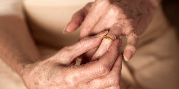 Old lady sitting with her hands in her lap touches the wedding ring on her finger as if fondly remembering her husband and happier days