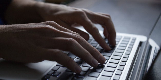 The hands of a young adult typing on the keyboard of a silver colored laptop. Backlit with high contrast.