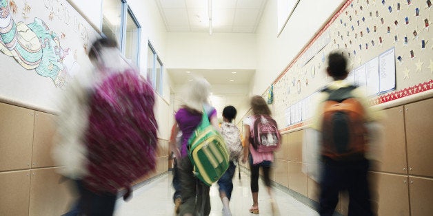 Young students with backpacks walking down hallway of elementary school