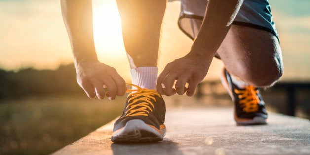 Man tying jogging shoes.A person running outdoors on a sunny day. The person is wearing black running shoes.Focus on a side view of two human hands reaching down to a athletic shoe.