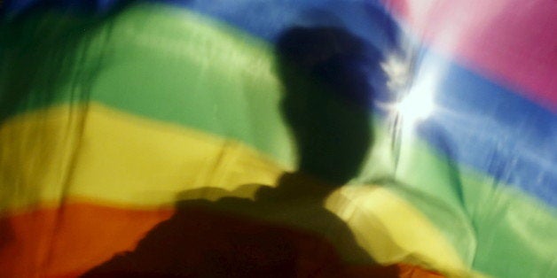 A gay man is silhoutted on a gay rainbow flag during a demonstration for gay rights in Hanoi, Vietnam, November 24, 2015. Whi