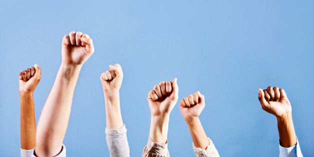 Multiracial clenched fists raised in the air could signify approval or defiance. Plenty of copy space against a sky blue background. 