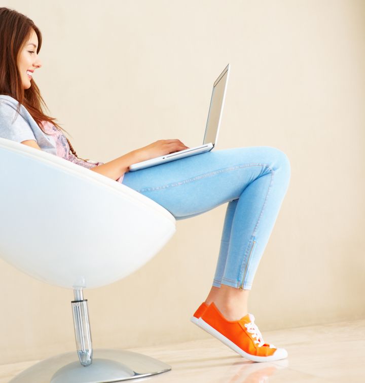 Side view of young woman sitting on ball chair using laptop