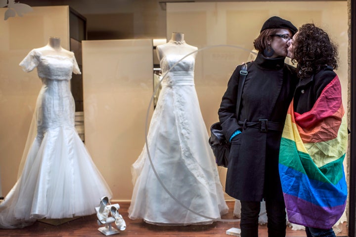 Two women, one wrapped in a rainbow flag, kiss in front of a wedding shop during a demonstration to support gay marriage and