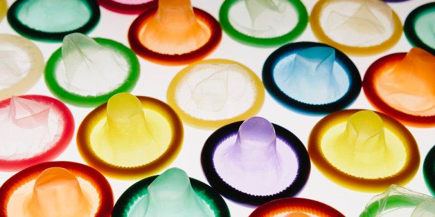 A large group of multi-colored condoms displayed on a white background. Laid out neatly.