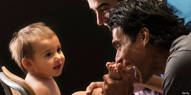 Two gay men couple posing with their child on black background