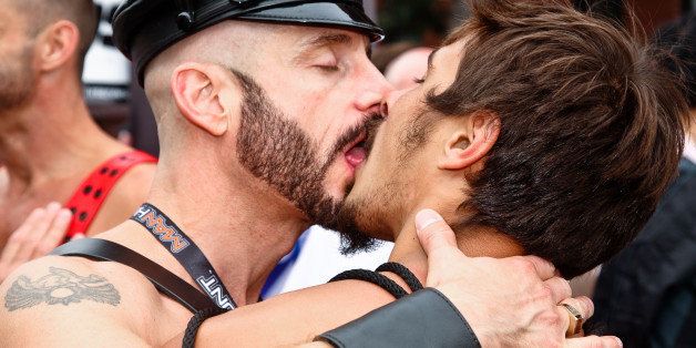 [UNVERIFIED CONTENT] Taken at Folsom Street Fair on the street in San Francisco. It is annual gay leather event. Two adult gay men kissing, with eyes closed, open mouth with visible tongue, and in full embrace. Both are shirtless, wearing leather. Both are muscular and white. The older man on the left has a shaved head, a full trimmed beard, is in his 40s, and is wearing a leather hat and a leather cuff on his right arm. The younger man on the right has a full head of hair, a partial untrimmed beard, and is in his 20s.