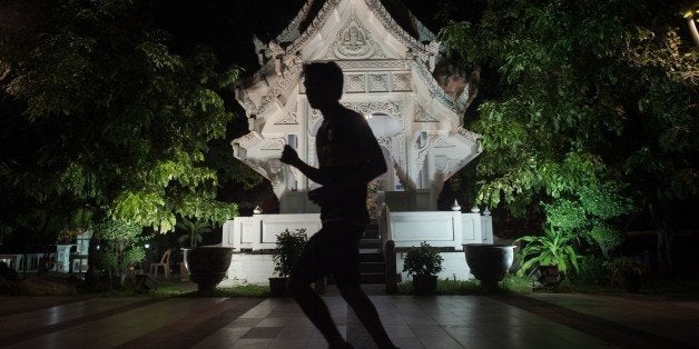 This picture taken on January 14, 2015 shows a man silhouetted as he jogs past an illuminated monument in Bangkok. AFP PHO